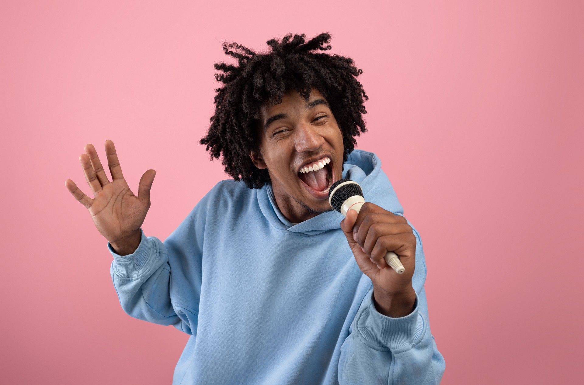 Rock star. Portrait of cool black teen guy singing song, using microphone, performing karaoke on pink background