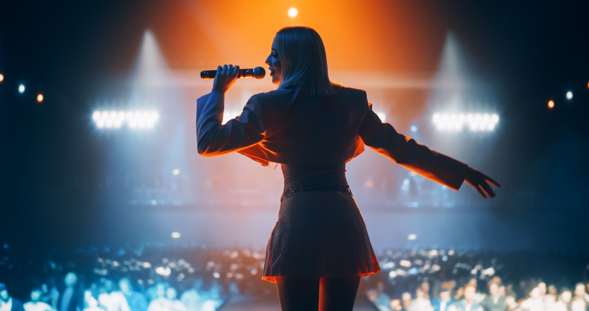 Energetic Pop Artist Performing on Stage in Pink Feminine Clothes. Excited Audience Listening to the Tunes and Being Illuminated by a Vibrant Light Show. Footage from the Back